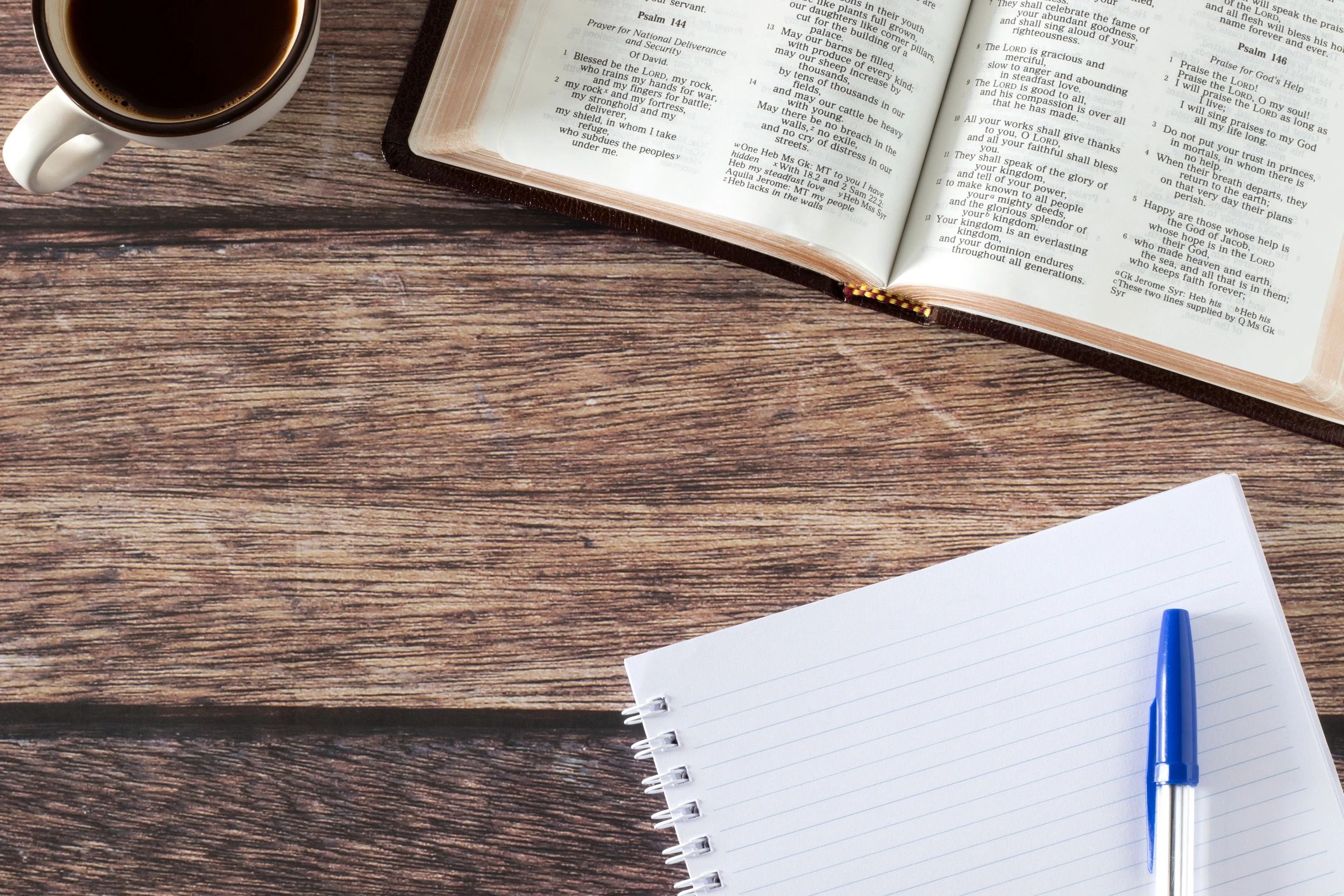 Open Bible and notebook with coffee on a wooden table.